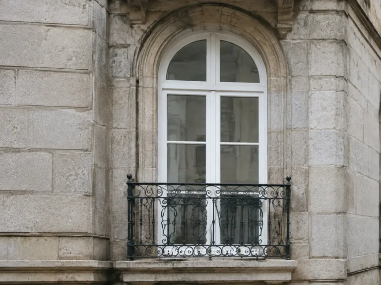 Ventana de arco con carpintería blanca y balcón de forja sobre fachada de granito de un edificio protegido